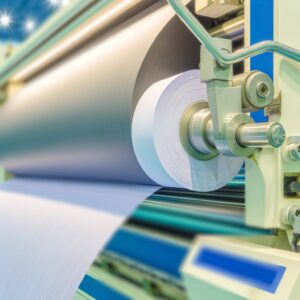 A close-up shot of a nonwoven fabric roll cutting machine in operation. The machine features a large roll of nonwoven fabric being fed into a cutting mechanism, with the resulting cut sheets neatly stacked on a conveyor belt.