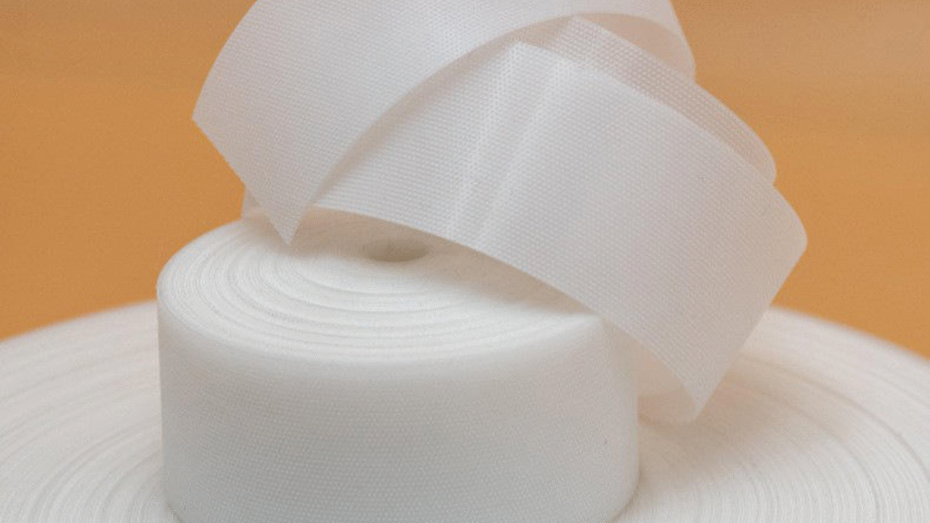 A lab technician is seen performing a peel strength test on a strip of magic frontal tape for diapers, ensuring its reliability for diaper fastening systems.