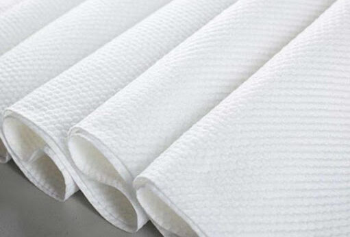 A detailed, close-up shot of a white roll of dot embossed spunlace fabric, highlighting its unique texture and high-quality finish.